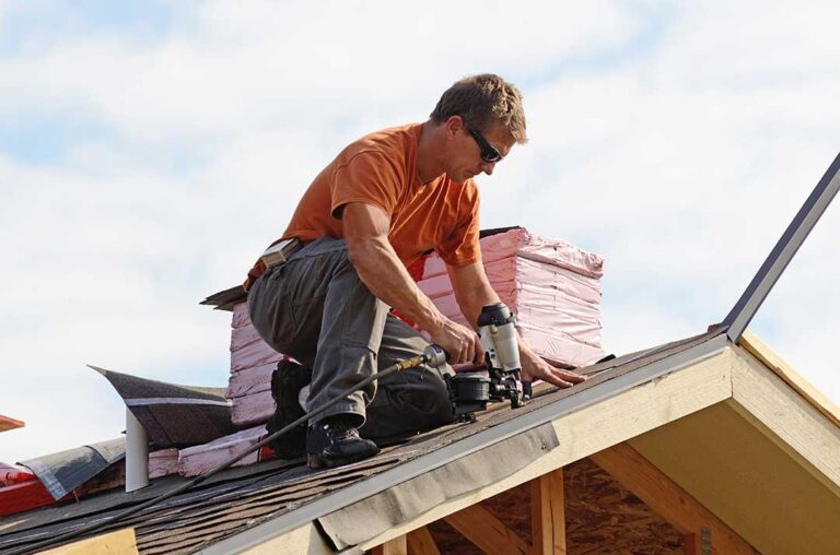 Homeowner inspecting attic insulation beneath roof rafters with daylight visible through a vented roof system.