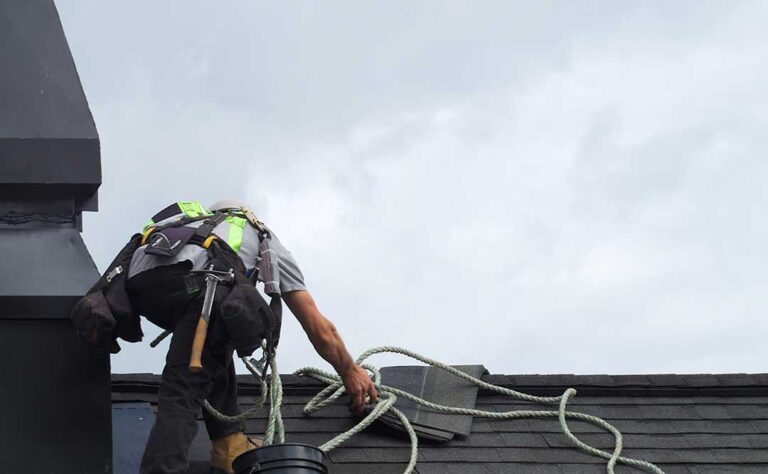 Homeowner reviewing roof warranty papers beside a window while a roof and ladder are visible outside.